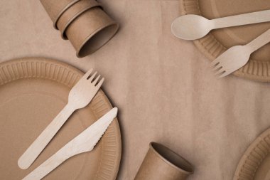 Plastik konsept kullanmayı bırak. Üst tepede tahta çatal bıçak takımının, kağıt bardakların ve el işi kağıt arka plan masasında izole tabakların fotoğrafı var.