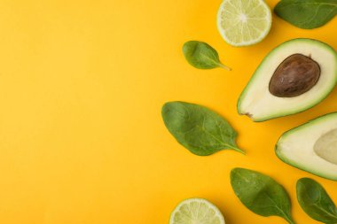 Üst tepede kesilmiş avokado, limon dilimleri ve bebek ıspanak yapraklarının sarı arka planda izole edilmiş fotoğrafı var.