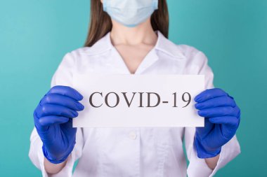 Elinde COVID 19 sosyal mesafe kağıdı olan mavi turkuaz arka planda yakın planda çekilmiş kadın doktor fotoğrafı.