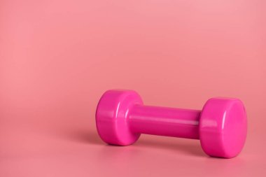 Antrenman konsepti. Pembe arkaplanda izole edilmiş pembe dambılın yakın plan fotoğrafı.
