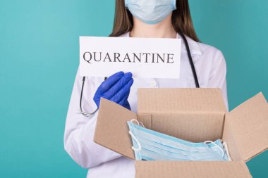 İnsani yardım kuryesi kendini soyutlama kavramına yardım ediyor. Mavi turkuaz arka planda, elinde bir kutu maske ve karantina kağıdı tutan eldivenli kadın doktorun yakın planda çekilmiş fotoğrafı.