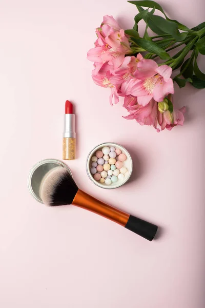 Make-up powder brush, powder in balls, red lipstick and beautiful pink bouquet of flowers. Womens make-up kit, gift for girl concept