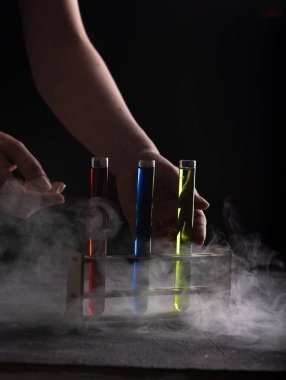 Kadın barmenin elleri cam tüplerle renkli içki servisi yapıyor. Duman ya da buhar. Koyu arkaplan, atmosfer çubuğu resmi