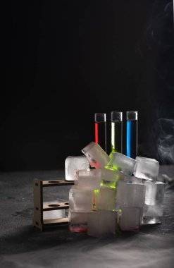 Cam tüplerde renkli içecekler, dumanlar, buharlar ve buz küpleri. Koyu arkaplan, kopyalama alanı olan atmosfer çubuğu resmi