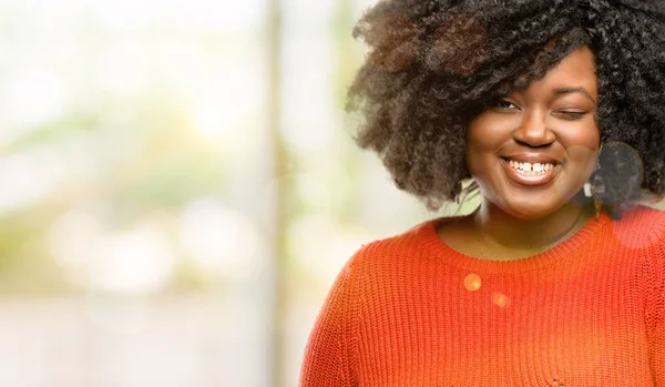 Beautiful african woman blinking eyes with happy gesture, outdoor