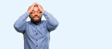 Sakallı stresli Afrikalı-Amerikalı adam el üzerinde mavi arka plan izole baş, yorgun ve sinirli tutmak