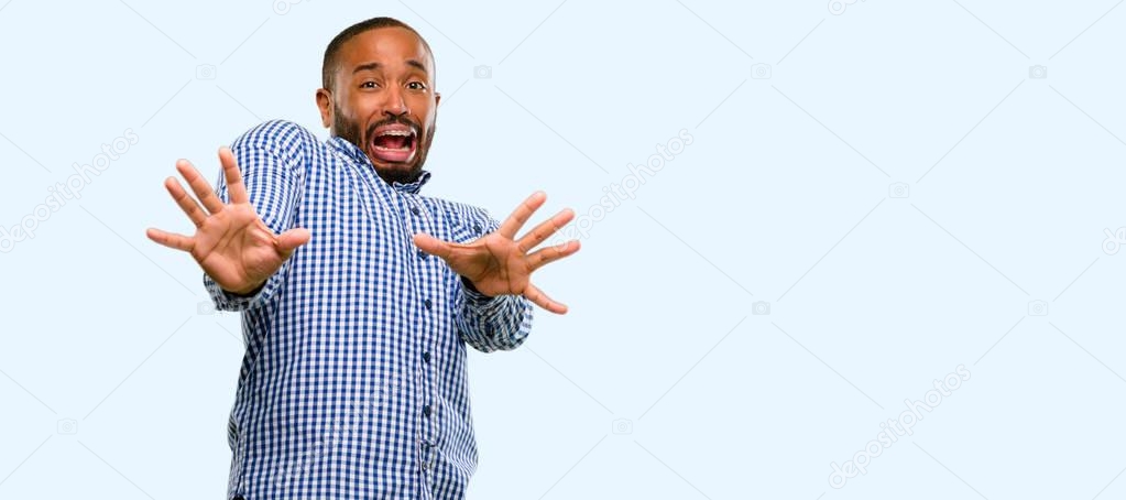African american man with beard disgusted and angry, keeping hands in stop gesture, as a defense, shouting isolated over blue background