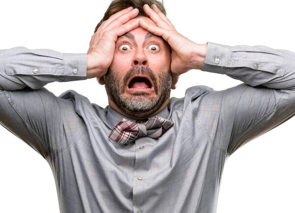 Middle age man, with beard and bow tie stressful keeping hands on head, terrified in panic, shouting isolated over white background
