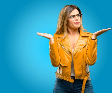 Güzel ve genç birbayan şüphe ifade, şaşırtmak ve merak ediyorum kavramı, belirsiz gelecekte omuzlarında shrugging, mavi arka plan