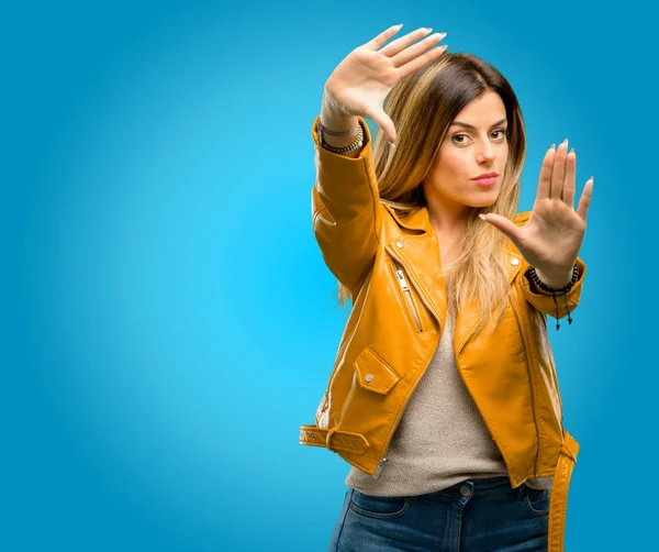 Beautiful young woman confident and happy showing hands to camera, composing and framing gesture, blue background