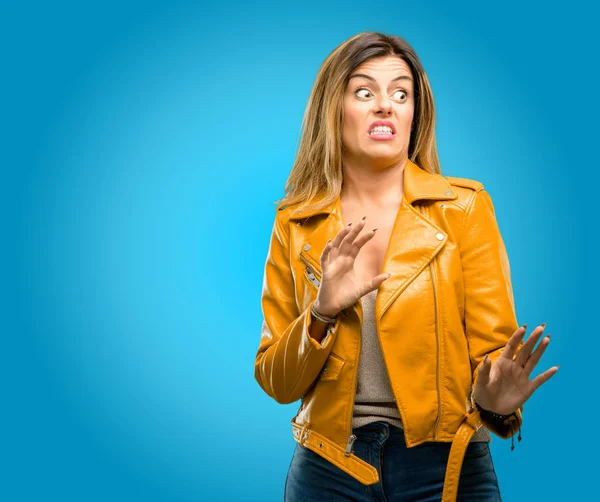 Beautiful young woman disgusted and angry, keeping hands in stop gesture, as a defense, shouting, blue background