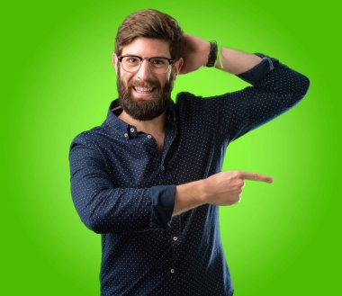 Yeşil arka plan üzerinde uzak yan parmağıyla işaret büyük sakallı genç hipster adam