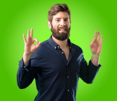 Meditasyon ve gevşeme yeşil arka plan üzerinde ifade iki eliyle ok işareti jest yapıyor büyük sakallı genç hipster adam