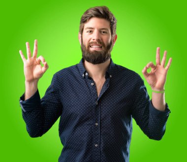 Meditasyon ve gevşeme yeşil arka plan üzerinde ifade iki eliyle ok işareti jest yapıyor büyük sakallı genç hipster adam