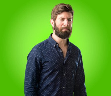 Yeşil arka plan üzerinde mutsuz ve üzgün üzgün ifade ile büyük sakallı genç hipster adam
