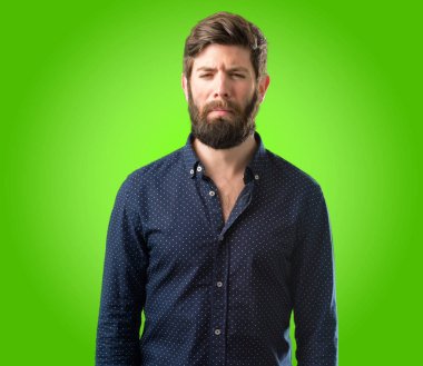 Yeşil arka plan üzerinde mutsuz ve üzgün üzgün ifade ile büyük sakallı genç hipster adam