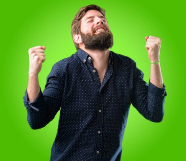 Mutlu ve heyecanlı kazanan jest ifade büyük sakallı genç hipster adam. Başarılı ve zafer, yeşil arka plan üzerinde zafer kutluyor