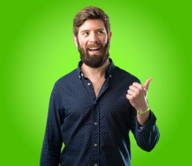 Yeşil arka plan üzerinde uzak yan parmağıyla işaret büyük sakallı genç hipster adam