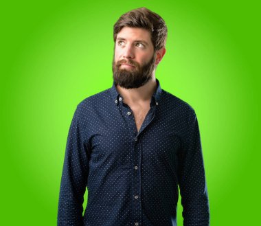 Büyük sakal şüphe ifade, adamla genç hipster şaşırtmak ve kavramı, yeşil arka plan üzerinde belirsiz gelecek merak ediyorum