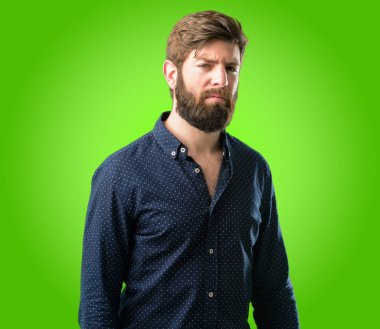 Büyük sakallı genç hipster adam rahatsız ve kızgın negatif duygu ifade, biriyle yeşil arka plan üzerinde rahatsız