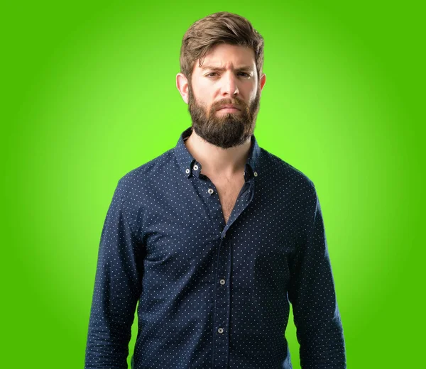 Büyük sakallı genç hipster adam rahatsız ve kızgın negatif duygu ifade, biriyle yeşil arka plan üzerinde rahatsız