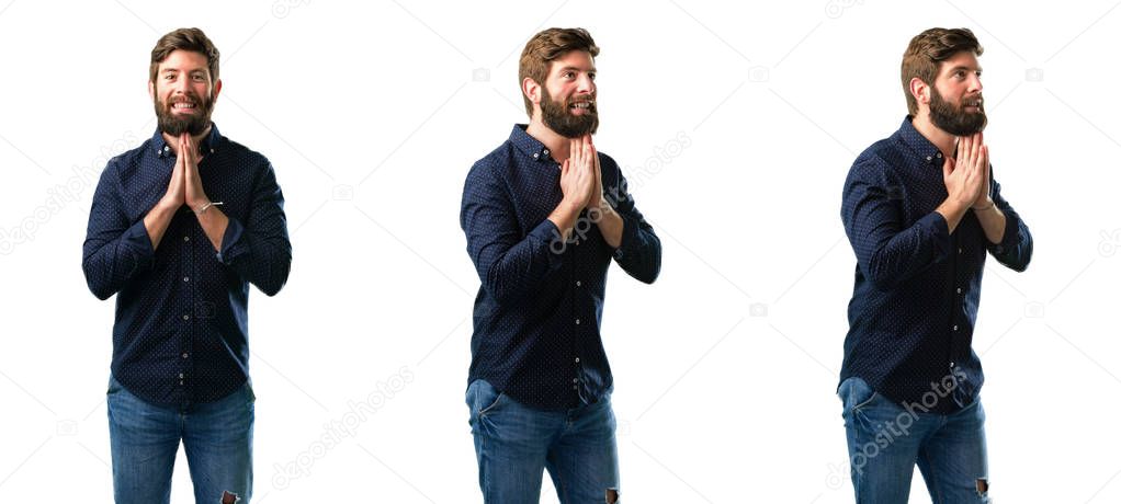 Young man with beard with hands together in praying gesture, expressing hope and please concept isolated over white background