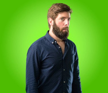 Şüpheci ve memnun olan büyük sakallı genç hipster adam bak ifade güvensizlik, şüphecilik ve şüphe yeşil arka plan üzerinde