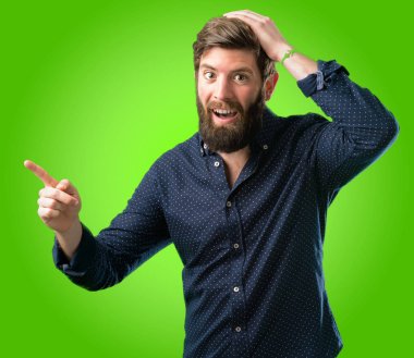 Yeşil arka plan üzerinde uzak yan parmağıyla işaret büyük sakallı genç hipster adam