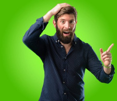 Yeşil arka plan üzerinde uzak yan parmağıyla işaret büyük sakallı genç hipster adam