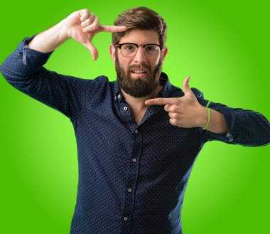 Kendinden emin ve mutlu eller fotoğraf makinesi için gösterilen, beste ve jest yeşil arka plan üzerinde çerçeveleme büyük sakallı genç hipster adam