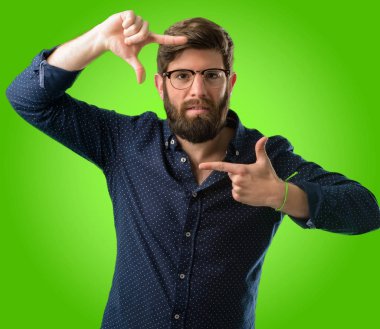 Kendinden emin ve mutlu eller fotoğraf makinesi için gösterilen, beste ve jest yeşil arka plan üzerinde çerçeveleme büyük sakallı genç hipster adam