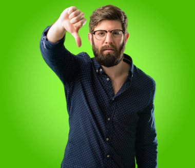 Büyük sakal gösteren başparmak sevmemek, mutsuz iz aşağı adamla genç hipster negatif ifade ve ret yeşil arka plan üzerinde