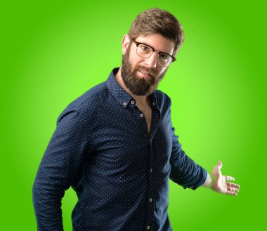 Kendinden emin ve mutlu bir büyük doğal büyük sakallı genç hipster adam gülümseme yeşil arka plan üzerinde girmek için davet