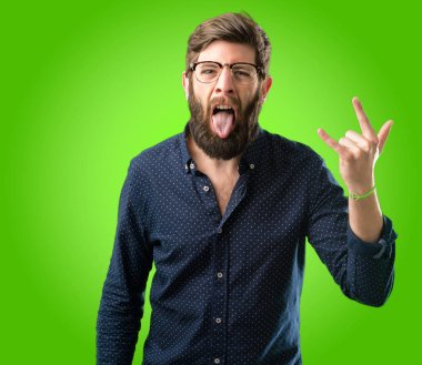 Rock simge elle yapma, bağırarak ve dilini çıkarmış yeşil arka plan üzerinde kutluyor büyük sakallı genç hipster adam