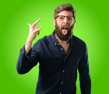 Rock simge elle yapma, bağırarak ve dilini çıkarmış yeşil arka plan üzerinde kutluyor büyük sakallı genç hipster adam