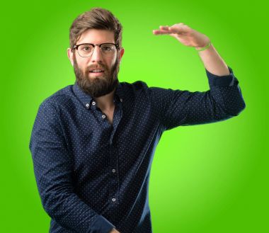 Bir şey boyutu kavram yeşil arka plan üzerinde tutan büyük sakallı genç hipster adam
