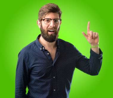 Yeşil arka plan üzerinde uzak yan parmak ile işaret büyük sakallı genç hipster adam