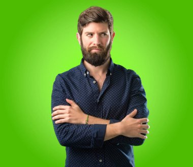 Büyük sakallı genç hipster adam rahatsız ve kızgın negatif duygu ifade, biriyle yeşil arka plan üzerinde rahatsız