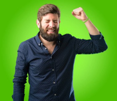 Mutlu ve heyecanlı kazanan jest ifade büyük sakallı genç hipster adam. Başarılı ve zafer, yeşil arka plan üzerinde zafer kutluyor