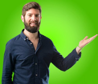 Bir şey yeşil arka plan üzerinde boş elinde tutan büyük sakallı genç hipster adam