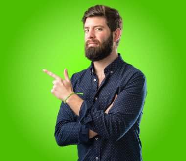 Yeşil arka plan üzerinde uzak yan parmak ile işaret büyük sakallı genç hipster adam