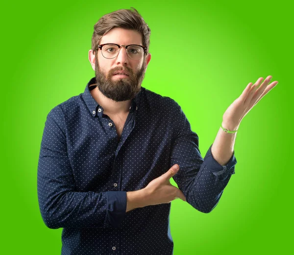 Büyük sakallı genç hipster adam rahatsız ve kızgın negatif duygu ifade, biriyle yeşil arka plan üzerinde rahatsız