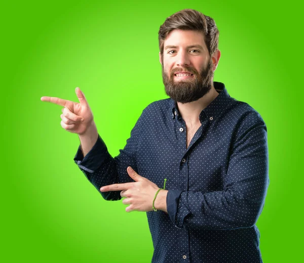 Yeşil arka plan üzerinde uzak yan parmak ile işaret büyük sakallı genç hipster adam