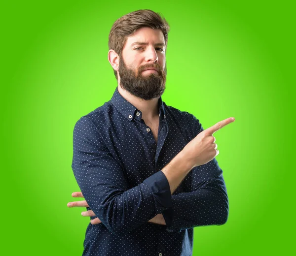 年轻的时髦的人与大胡子指向一边用手指在绿色背景上 — 图库照片