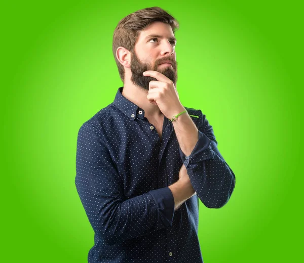 年轻的时髦男子与大胡子思考和寻找表达怀疑和怀疑的绿色背景 — 图库照片