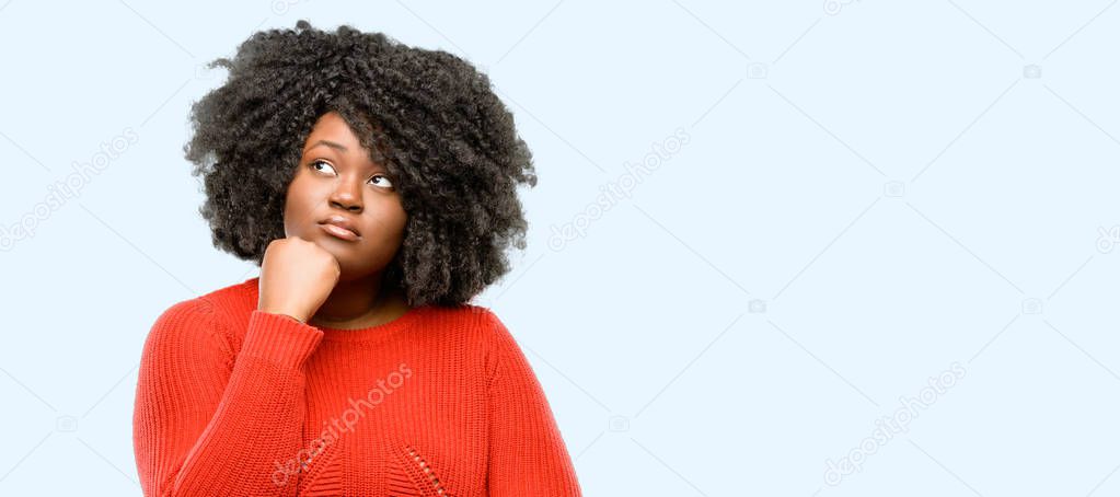 Beautiful african woman thinking and looking up expressing doubt and wonder, blue background