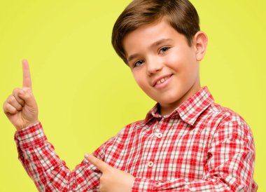 Sarı arka plan üzerinde uzak yan parmak ile işaret yeşil gözlü yakışıklı yürümeye başlayan çocuk