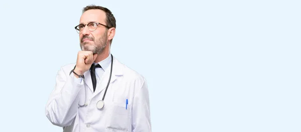 医者年配の男性 医療の専門的な思考と疑いを表現する見上げると青い背景上孤立したのだろうか — ストック写真