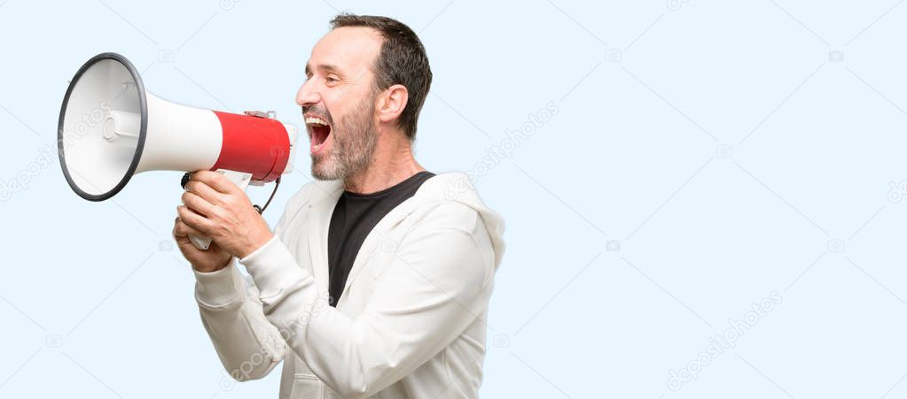 Middle age man wearing sportswear communicates shouting loud holding a megaphone, expressing success and positive concept, idea for marketing or sales isolated over blue background