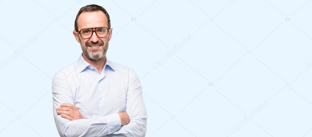 Middle age man with glasses with crossed arms confident and happy with a big natural smile laughing isolated over blue background